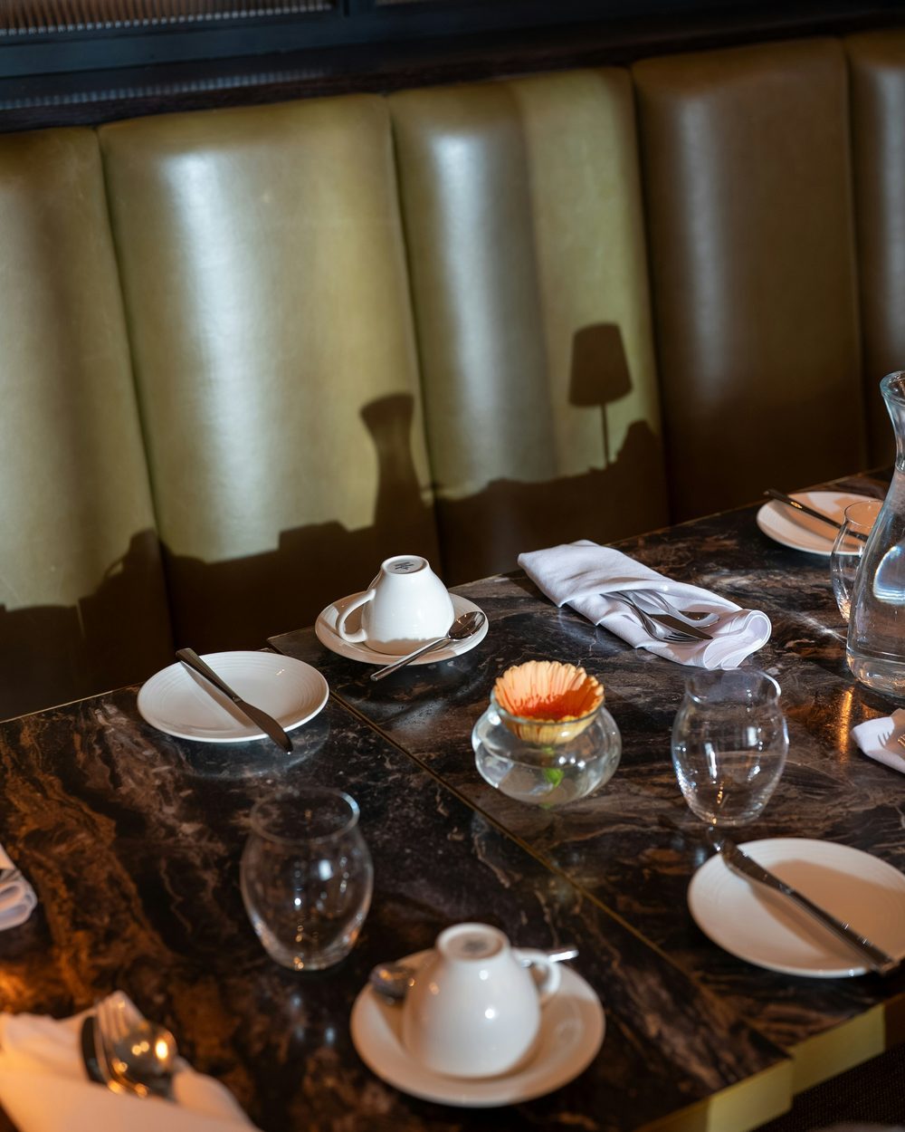 Table dressée sur marbre sombre, banquette de cuir vert